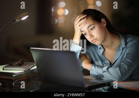 Besorgter Tele-Mitarbeiter, der nachts zu Hause den Laptop überprüft Stockfoto