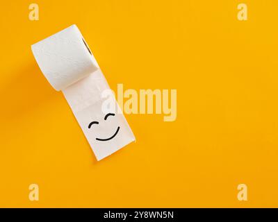 Hochwertiges und komfortables Toilettenpapier. Weiße Toilettenpapierrolle mit lustigem lächelndem Gesicht, das auf hellgelbem Hintergrund mit Kopierraum liegt. Stockfoto