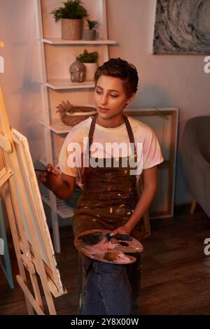 Eine junge Frau in einer Schürze widmet sich zuhause der Malerei und zeigt ihr künstlerisches Talent und ihre Leidenschaft für Kreativität. Stockfoto