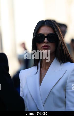 Eine Einladung mit einem langen weißen klassischen Mantel und einer kleinen Clutch-Handtasche in Schwarz von Chanel auf der Elie Saab Show für die Paris Fashion Week SS25 Stockfoto