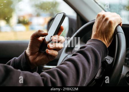 Männlicher Fahrer fährt Auto und schreibt SMS auf dem Handy, selektiv Stockfoto