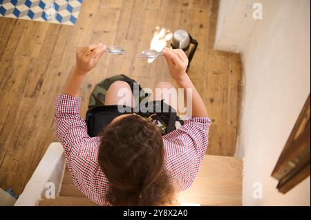 Blick von oben auf eine Frau, die auf einer Treppe sitzt und eine Sonnenbrille mit Holzboden und geometrischen Fliesen in der Nähe inspiziert. Zwanglose, entspannte Atmosphäre. Stockfoto