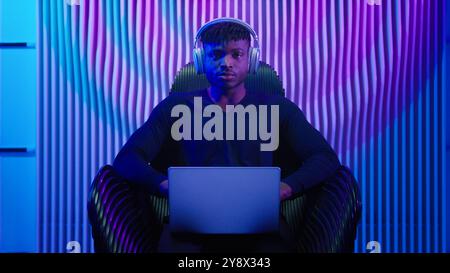 Afroamerikanischer Mann Guy männlicher Coder Gamer Programmierer in Stuhl tragen Kopfhörer mit Laptop Online Arbeit Krypto Software spielen Internet-Spiel modern Stockfoto