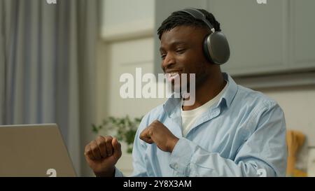 Glücklicher lustiger lächelnder Afroamerikaner Mann zu Hause genießt Musik hören Song hören Audio in kabellosen Kopfhörern Ohrhörern mit Laptop Stockfoto