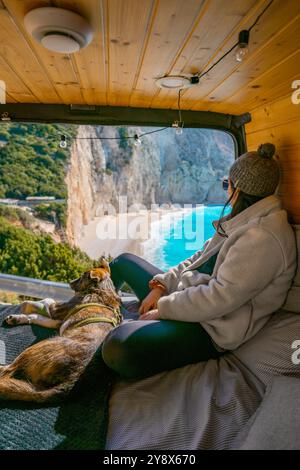 Frau und Hund auf dem Bett des Wohnwagens und schauen auf den Strand mit türkisfarbenem Wasser Stockfoto