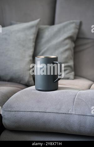 Eleganter grauer Becher auf weichem Sofa mit Kissen. Stockfoto