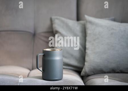 Eleganter grauer Becher auf weichem Sofa mit Kissen. Stockfoto