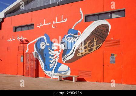 Ein leuchtend rotes Gebäude mit einem großen blauen Sneaker-Wandgemälde vor einem klaren blauen Himmel in der O'Village Mall in casablanca Stockfoto