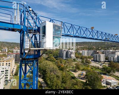 Ein blauer Kran ragt über einer Baustelle mit modernen Gebäuden und einem Park im Hintergrund unter klarem Himmel Stockfoto