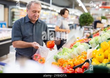 Reifer Kunde wählt Paprika mit Interesse an der Lebensmittelabteilung eines Supermarktes aus Stockfoto