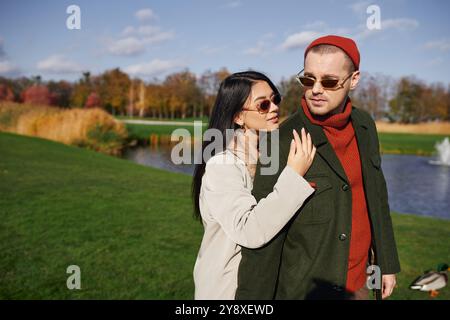 Ein Paar umarmt sich warm, in Herbstkleidung gekleidet, während es von farbenfrohen Herbstlaub umgeben ist. Stockfoto