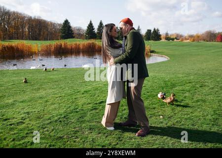 Ein liebevolles Paar genießt einen warmen Moment zusammen, umgeben von Herbstfarben in der Nähe eines ruhigen Teichs. Stockfoto