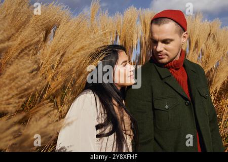 Ein liebevolles Paar umarmt sich herzlich, umgeben von goldenem Herbstlaub unter hellem Himmel. Stockfoto