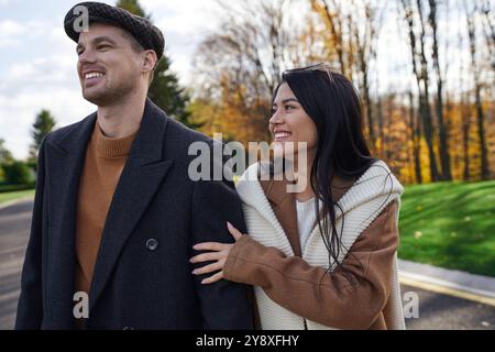 Ein Paar spaziert Hand in Hand durch einen Park, um die Wärme des Herbstes in ihren Outfits zu genießen. Stockfoto