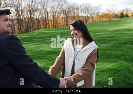 Ein liebevolles Paar lacht, während es in einer wunderschönen Herbstlandschaft Hände hält. Stockfoto