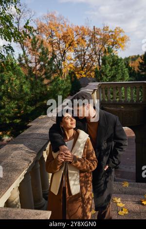 In warme Kleidung gehüllt, teilt ein Paar einen zarten Moment, umgeben von Herbstlaub. Stockfoto