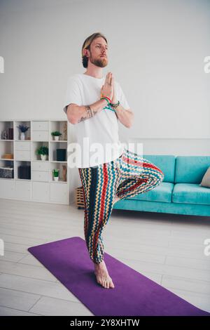 Vertikales Foto in voller Größe des netten jungen Mannes Matte Yoga Übungskleidung stilvoller Pyjama modernes helles gemütliches Inneres flach drinnen Stockfoto