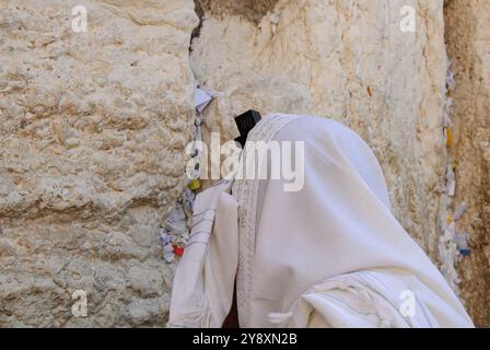 Ein Mann, der Tefillin trägt und mit einem Tallit oder einem jüdischen Gebetschal bedeckt ist, betet neben den Steinen der Westmauer in Jerusalem, Israel. Stockfoto