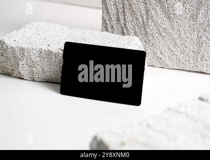 Ein raffiniertes Modell mit schwarzer Karte, das elegant vor einem sauberen weißen Steinhintergrund dargestellt wird. Dieses minimalistische Design unterstreicht das schlanke Design Stockfoto