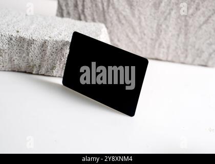 Ein raffiniertes Modell mit schwarzer Karte, das elegant vor einem sauberen weißen Steinhintergrund dargestellt wird. Dieses minimalistische Design unterstreicht das schlanke Design Stockfoto