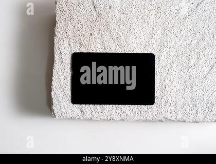 Ein raffiniertes Modell mit schwarzer Karte, das elegant vor einem sauberen weißen Steinhintergrund dargestellt wird. Dieses minimalistische Design unterstreicht das schlanke Design Stockfoto