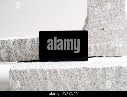 Ein raffiniertes Modell mit schwarzer Karte, das elegant vor einem sauberen weißen Steinhintergrund dargestellt wird. Dieses minimalistische Design unterstreicht das schlanke Design Stockfoto
