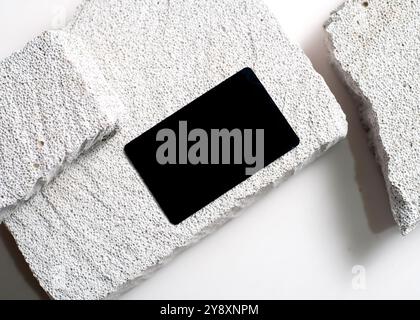 Ein raffiniertes Modell mit schwarzer Karte, das elegant vor einem sauberen weißen Steinhintergrund dargestellt wird. Dieses minimalistische Design unterstreicht das schlanke Design Stockfoto