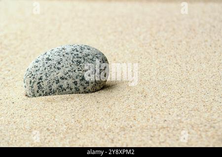 Einzelner Stein auf Strandsand mit anpassbarem Platz für Text oder Ideen. Stockfoto