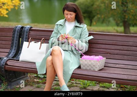 Eine Frau ist in der Kunst des Strickens vertieft, ihre Hände arbeiten mit rosa Garn und Nadeln. Eine Frau strickt mit Nadeln aus Fäden. Ein Stricker, der sich mit der manuellen Kreativarbeit beschäftigt Stockfoto