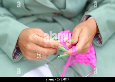 Eine Frau ist in der Kunst des Strickens vertieft, ihre Hände arbeiten mit rosa Garn und Nadeln. Eine Frau strickt mit Nadeln aus Fäden. Ein Stricker, der sich mit der manuellen Kreativarbeit beschäftigt Stockfoto
