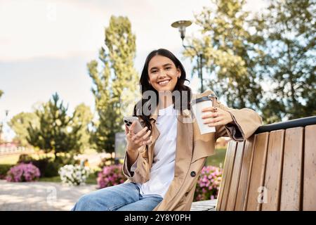 Eine fröhliche Frau genießt im Herbst Kaffee und SMS auf einer Parkbank. Stockfoto