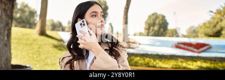 Eine schöne Frau in kuscheliger Herbstkleidung redet auf ihrem Telefon unter fallenden Blättern. Stockfoto