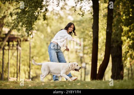 Eine junge Frau in warmen Herbstkleidung schlendert glücklich mit ihrem Hund im Park. Stockfoto