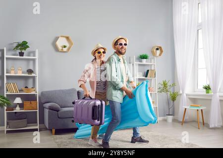 Fröhliches Paar in Sonnenbrille, Koffer und Luftmatratze sind bereit für Sommerabenteuer. Stockfoto