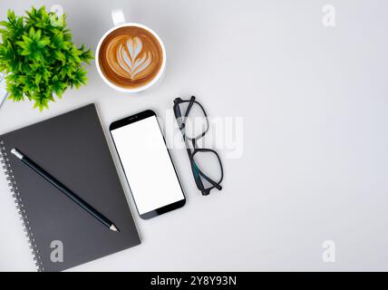 Draufsicht auf einen modernen Arbeitsplatz mit Smartphone mit leerem Bildschirm, Kaffeetasse, Notebook, Bleistift, Brille. Bürosituation mit Tastatur und Zubehör Stockfoto