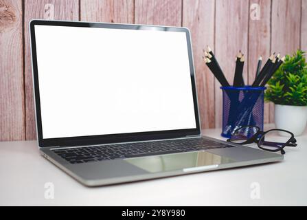 Laptop mit leerem Bildschirm auf weißem Tisch und Bürobedarf auf hölzernem Hintergrund. Platz zum Kopieren des Textes. Arbeitsbereich und Kopierbereich. Schreibtisch mit aus Stockfoto