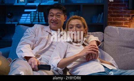 Multirassische Paare sehen sich abends einen Film an diversen verheirateten asiatischen Mann und kaukasische Frau glückliche Familie multiethnische koreanische Ehemann und Ehefrau Stockfoto