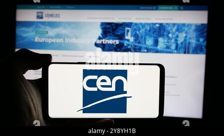 Person mit Smartphone und Logo des Europäischen Komitees für Normung (CEN) auf dem Bildschirm vor der Website. Schwerpunkt auf dem Display des Telefons. Stockfoto