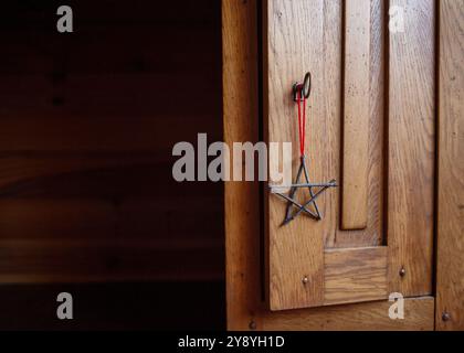 Handgefertigtes Sternenschmuck aus Zweigen, die an einer Holztür hängen, mit einer roten Schnur. Rustikale Weihnachtsdekoration in einem Zuhause. Winter holi Stockfoto