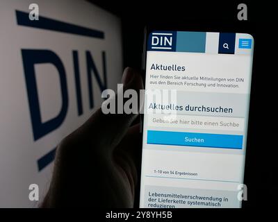 Handyhalter mit Webseite des Deutschen Instituts für Normung e.V. (DIN) auf dem Bildschirm vor dem Logo. Konzentrieren Sie sich auf die Mitte des Telefondisplays. Stockfoto