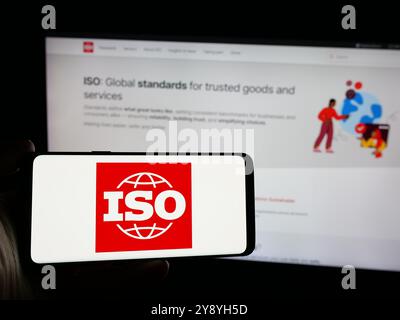 Person, die ein Smartphone mit dem Logo der Internationalen Organisation für Normung (ISO) auf dem Bildschirm vor der Website hält. Schwerpunkt auf dem Display des Telefons. Stockfoto