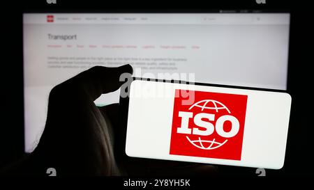 Person, die ein Mobiltelefon mit dem Logo der Internationalen Organisation für Normung (ISO) auf dem Bildschirm und der Website hält. Schwerpunkt auf dem Display des Telefons. Stockfoto