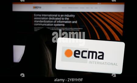 Person mit Mobiltelefon und Logo der Normungsorganisation Ecma International auf dem Bildschirm vor der Webseite. Schwerpunkt auf dem Display des Telefons. Stockfoto