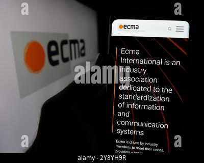 Person mit Smartphone und Website der Normungsorganisation Ecma International auf dem Bildschirm vor dem Logo. Konzentrieren Sie sich auf die Mitte des Telefondisplays. Stockfoto