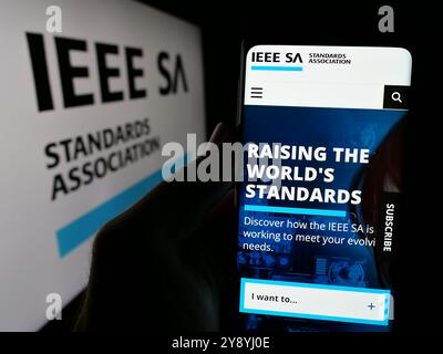 Person mit Mobiltelefon und Website der IEEE Standards Association auf dem Bildschirm vor dem Logo. Konzentrieren Sie sich auf die Mitte des Telefondisplays. Stockfoto