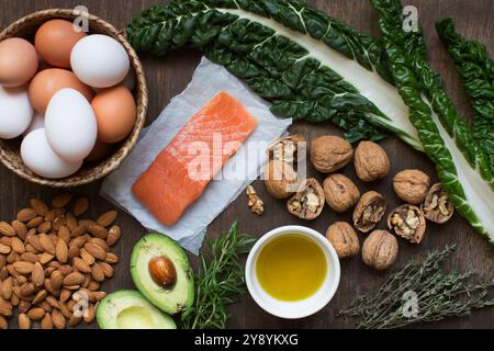 Inhaltsstoffe einer gesunden mediterranen Ernährung. Flach auf dunklem Holz mit frischem Lachs, Eiern, Walnüssen, Mandeln, Avocado, Mangold und Kräuter. Stockfoto