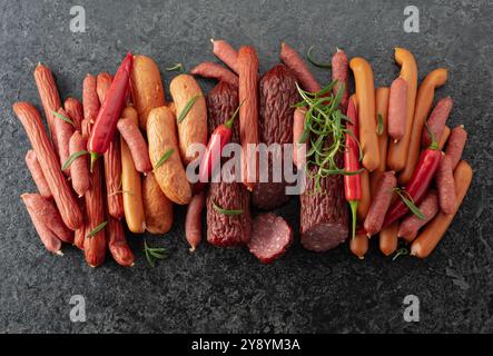 Verschiedene Trocken- und Räucherwürste mit roter Paprika und Rosmarin auf einem Steintisch. Draufsicht, Kopierraum. Stockfoto