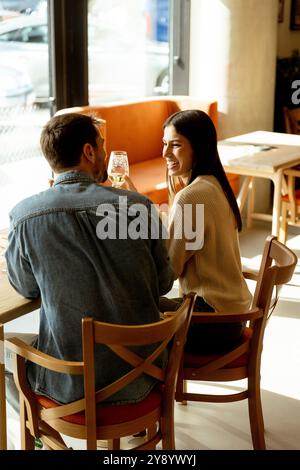 Ein Paar teilt sich einen freudigen Moment in einem Café und schlürft erfrischende Getränke, während er an einem Holztisch sitzt, umgeben von warmem Sonnenlicht und einem einladenden atmos Stockfoto