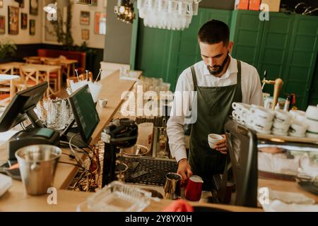 In einem warmen und einladenden Café gießt ein engagierter Barista fachmännisch Milch in eine Kaffeetasse und sorgt so für ein angenehmes Erlebnis für Gäste. Stockfoto