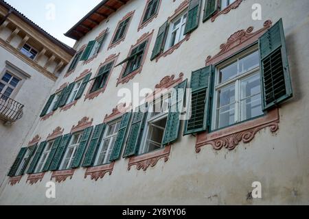 Ein Gebäude mit alten grünen Fensterläden und braunen Stuckfenstern, Meran, Norditalien. Stockfoto